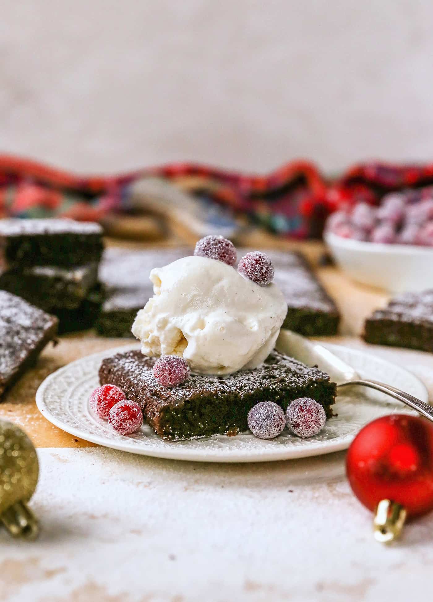 Gingerbread brownies are moist and fudgy, with a touch of molasses and warm spices. A fun holiday twist on a traditional brownie recipe! a gingerbread brownie on a plate with sugared cranberries and a scoop of ice cream