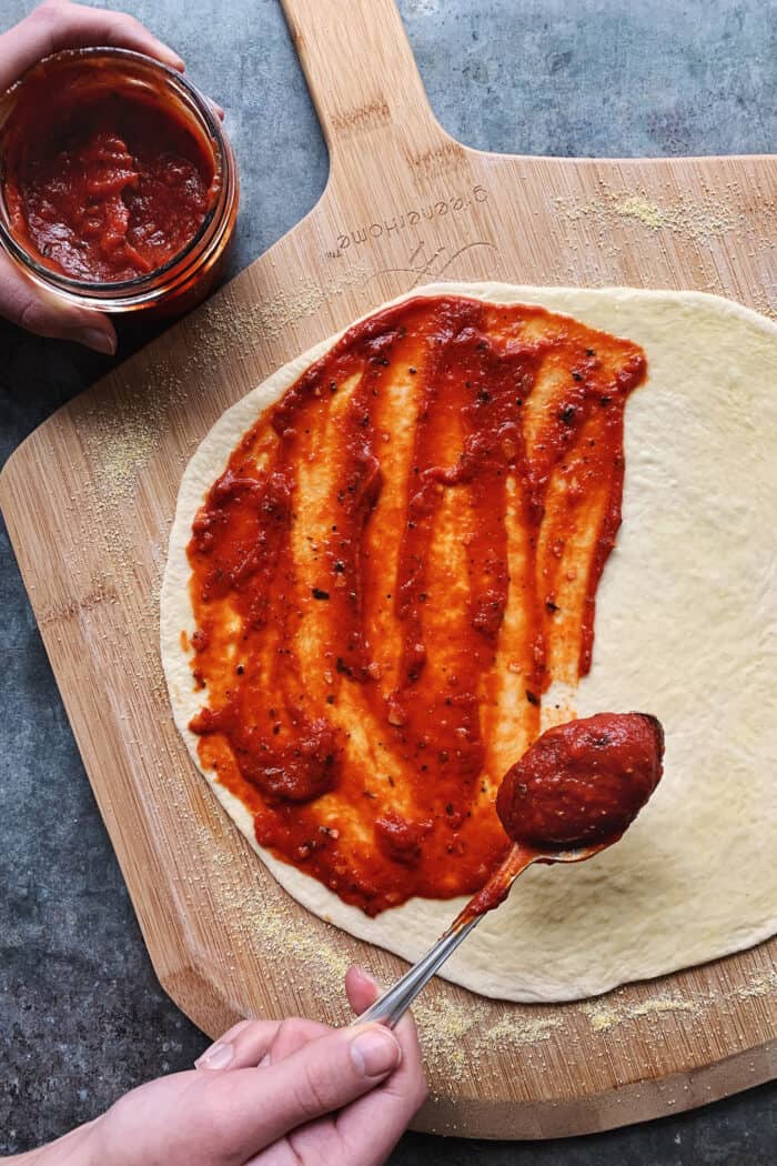 An easy recipe for the best homemade pizza sauce. It's a thick, tasty red sauce with fresh tomato flavor, made from simple ingredients! spooning red sauce onto pizza dough