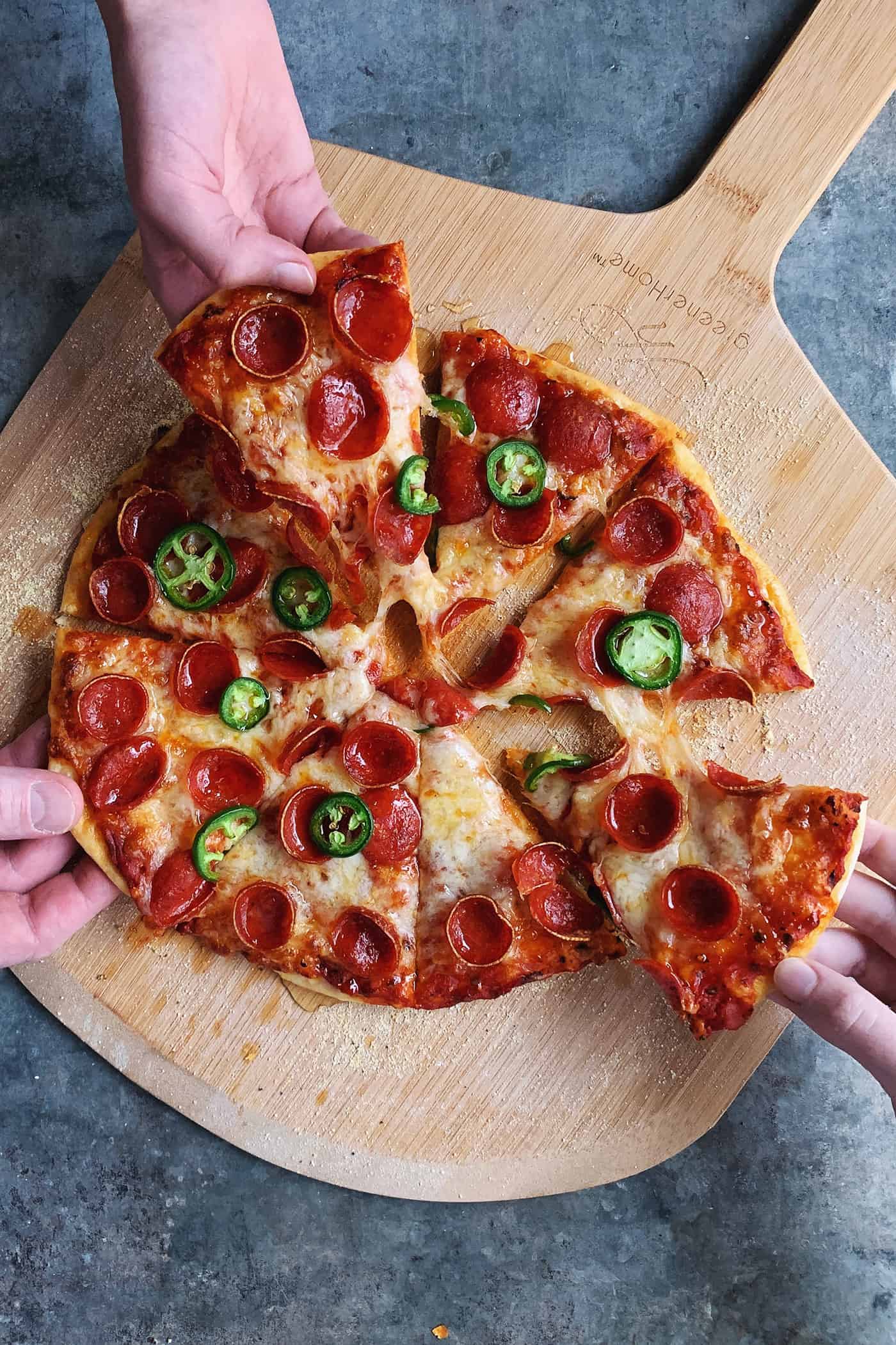 An easy recipe for the best homemade pizza sauce. It's a thick, tasty red sauce with fresh tomato flavor, made from simple ingredients! three hands pulling pieces of pizza off of a pizza peel
