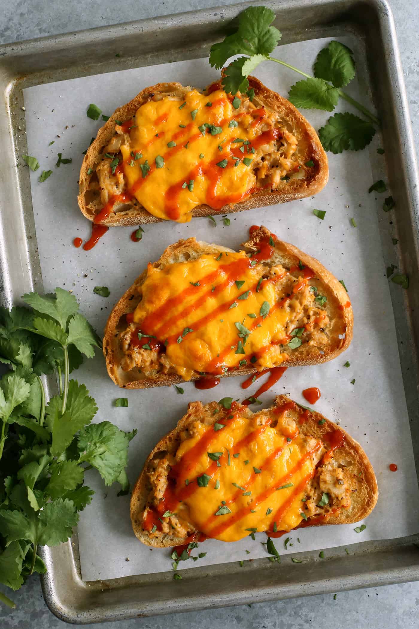 This spicy tuna melt recipe is a quick, easy hot sandwich with tuna, melty cheese, and spicy sriracha made warm and toasty in the oven! overhead photo of sriracha tuna melt sandwiches