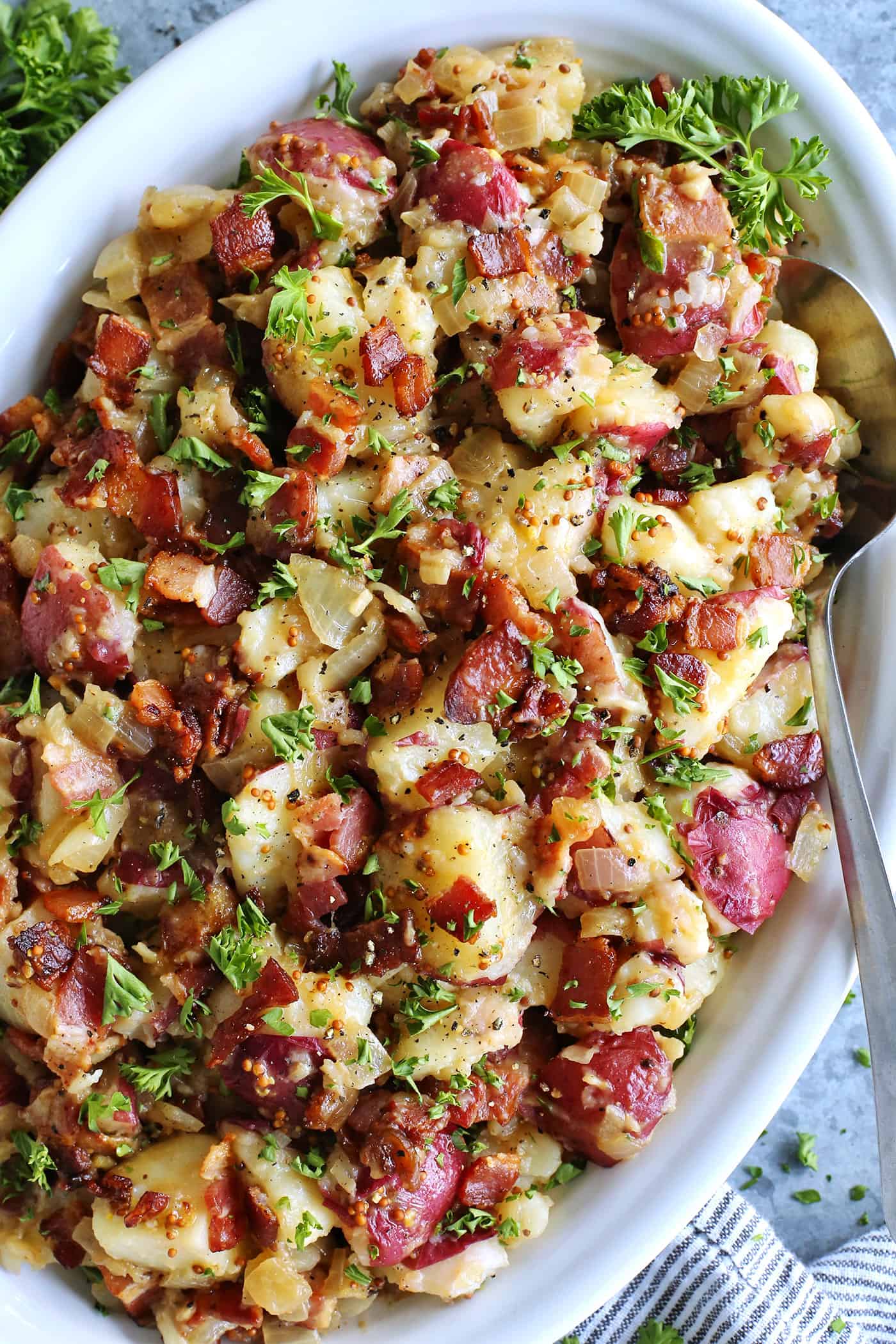 This warm German potato salad recipe combines tender red potatoes with bites of crispy bacon in a tangy vinegar and mustard dressing. German warm potato salad on a white platter