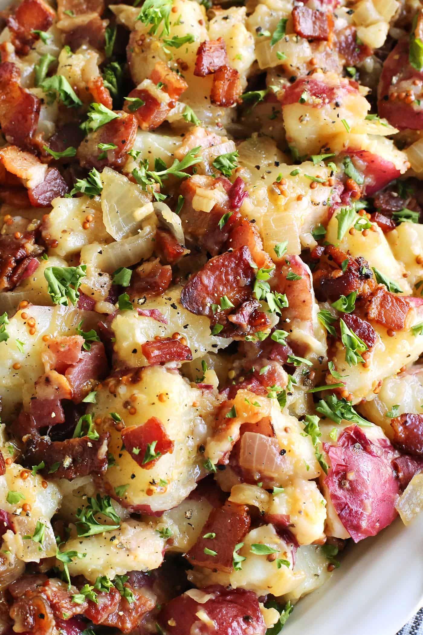 This warm German potato salad recipe combines tender red potatoes with bites of crispy bacon in a tangy vinegar and mustard dressing. close-up photo of German potato salad that shows the bacon pieces and whole grain mustard