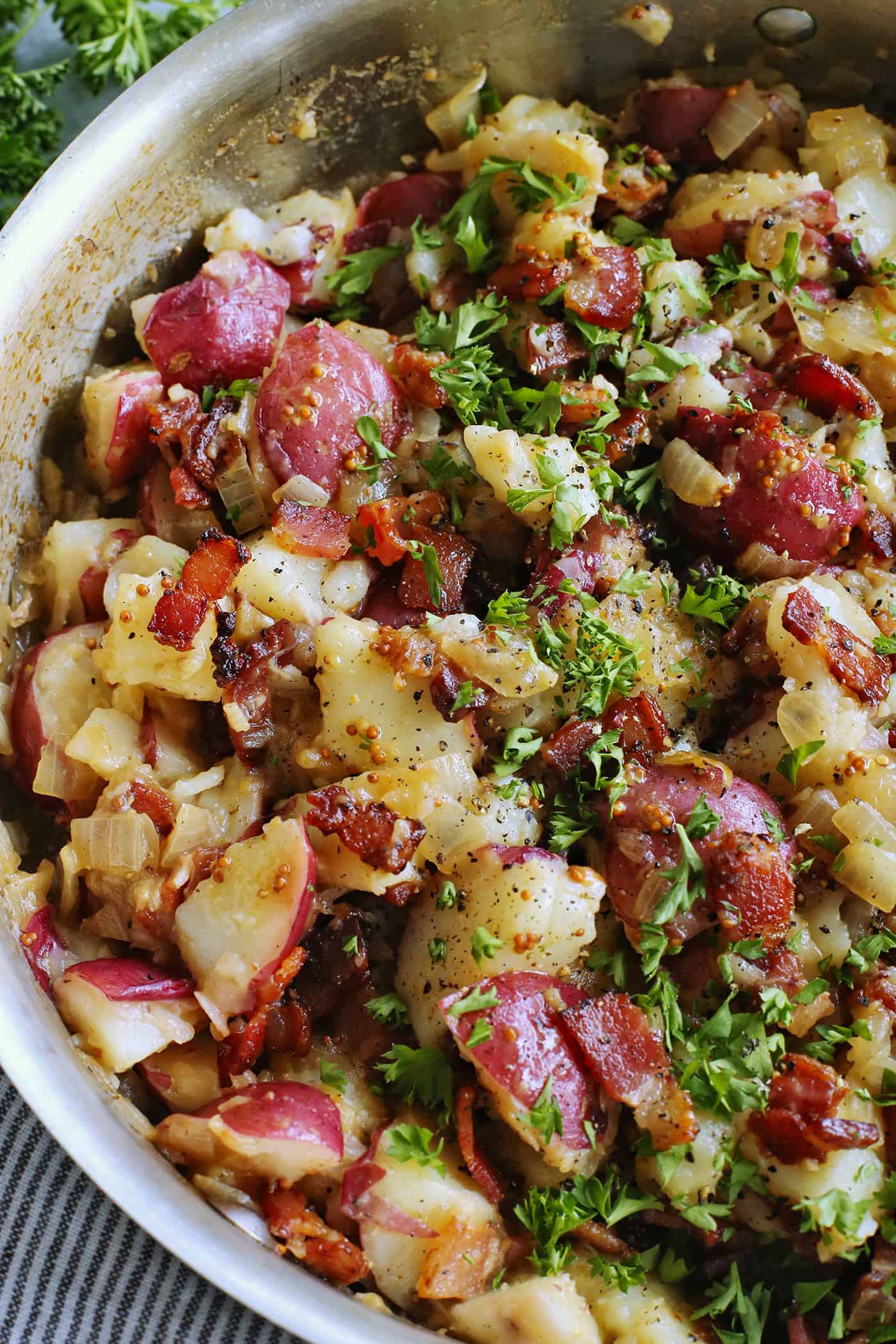 This warm German potato salad recipe combines tender red potatoes with bites of crispy bacon in a tangy vinegar and mustard dressing. German potato salad in a large skillet