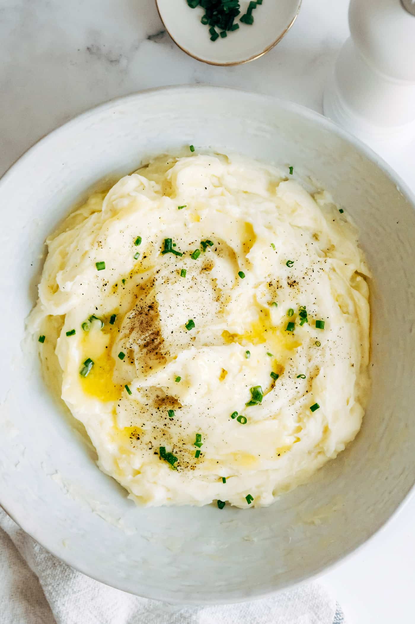 A serving bowl of homemade mashed potatoes with chives on top.