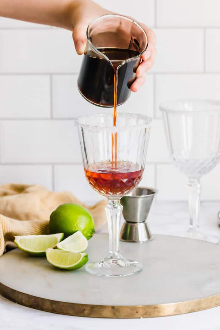 Mexican Coffee is a decadent dessert cocktail that's served hot. With tequila, Kahlua, and whipped cream, this recipe is a fun and beautiful way to top off a meal! pouring coffee into a stemmed glass with liqueurs