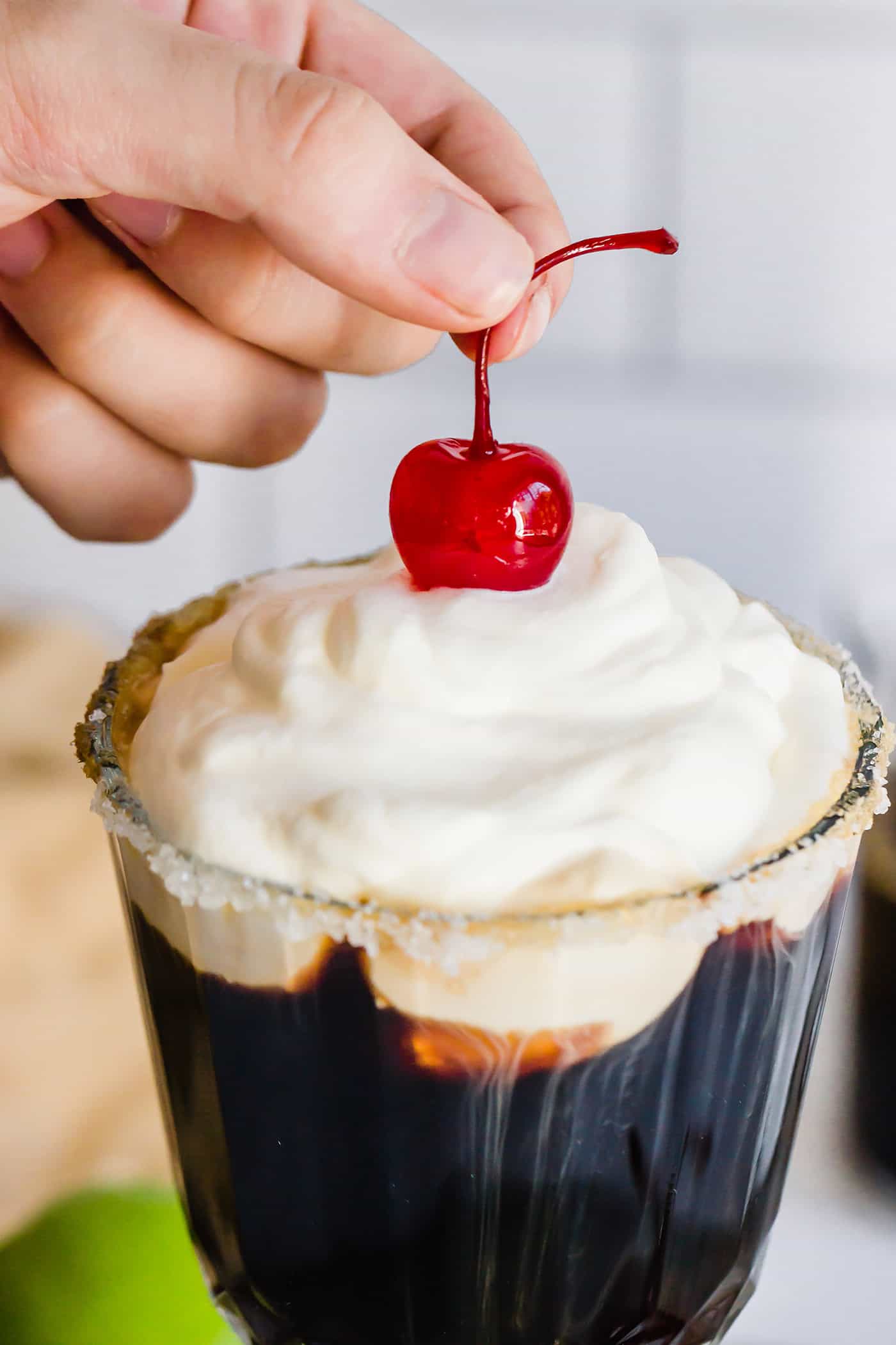 Mexican Coffee is a decadent dessert cocktail that's served hot. With tequila, Kahlua, and whipped cream, this recipe is a fun and beautiful way to top off a meal! pressing a stemmed cherry into the whipped cream topping on a Mexican coffee
