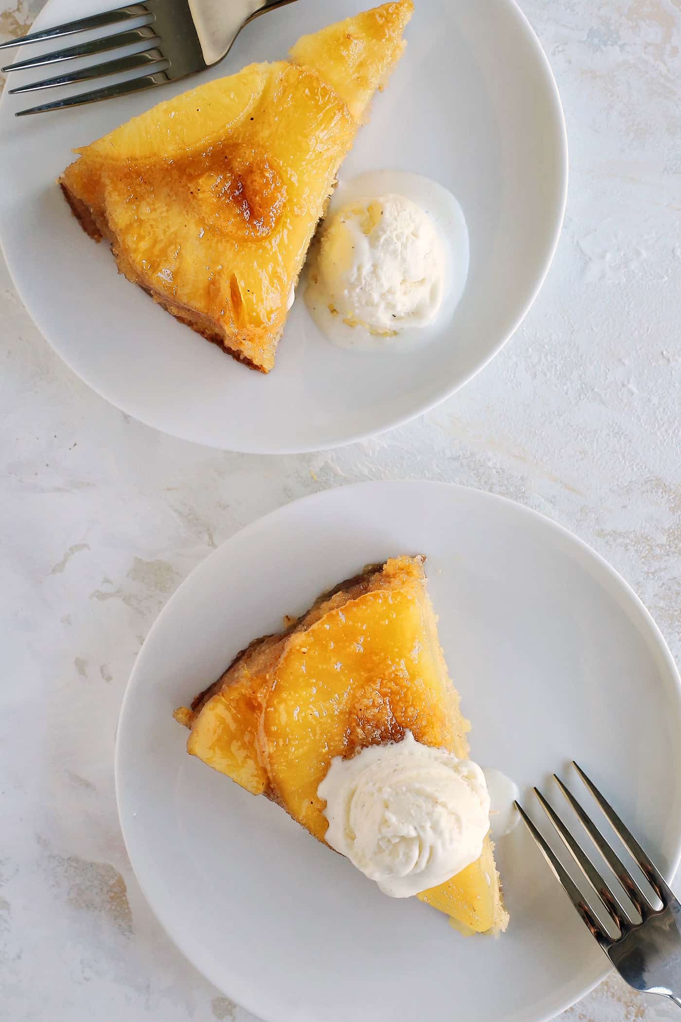 Overhead view of slices of pineapple upside-down cake with scoops of vanilla ice cream on small white plates.
