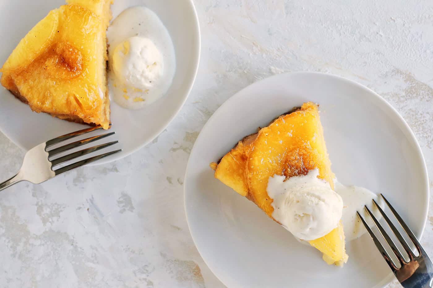 Overhead view of slices of pineapple upside-down cake with scoops of vanilla ice cream on small white plates.