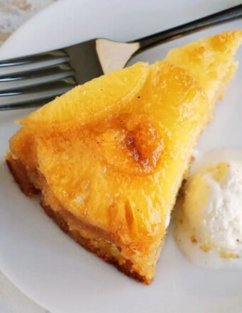 Close up of a slice of homemade pineapple upside down cake next to a scoop of ice cream on a plate, with a fork.