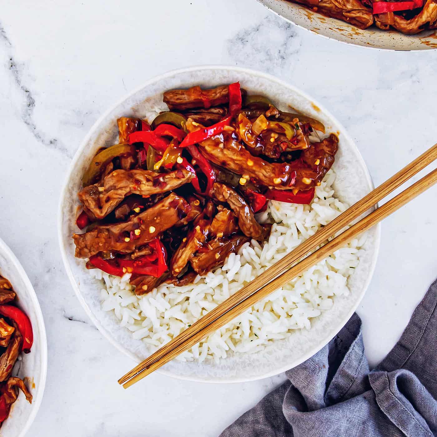 This copycat Beijing beef recipe had tender beef, peppers, and onions tossed in a sweet-spicy homemade sauce. It's even better than takeout! a white bowl with rice and Beijing beef, plus wooden chopsticks