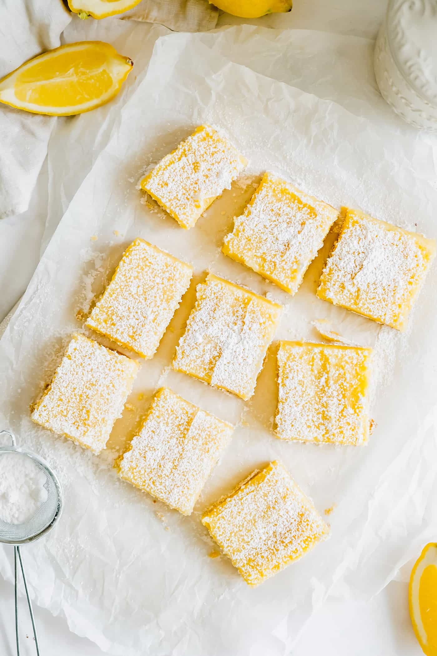 This easy lemon bars recipe is loaded with fresh lemon flavor in a buttery shortbread crust. Only 4 ingredients in the lemon curd filling! Lemon bars cut and sprinkled with powdered sugar, on a piece of white parchment paper