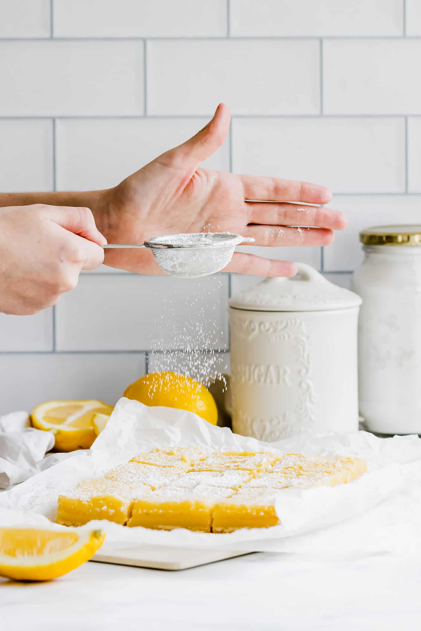 This easy lemon bars recipe is loaded with fresh lemon flavor in a buttery shortbread crust. Only 4 ingredients in the lemon curd filling! hands sprinkling powdered sugar over cut lemon bars on a piece of parchment