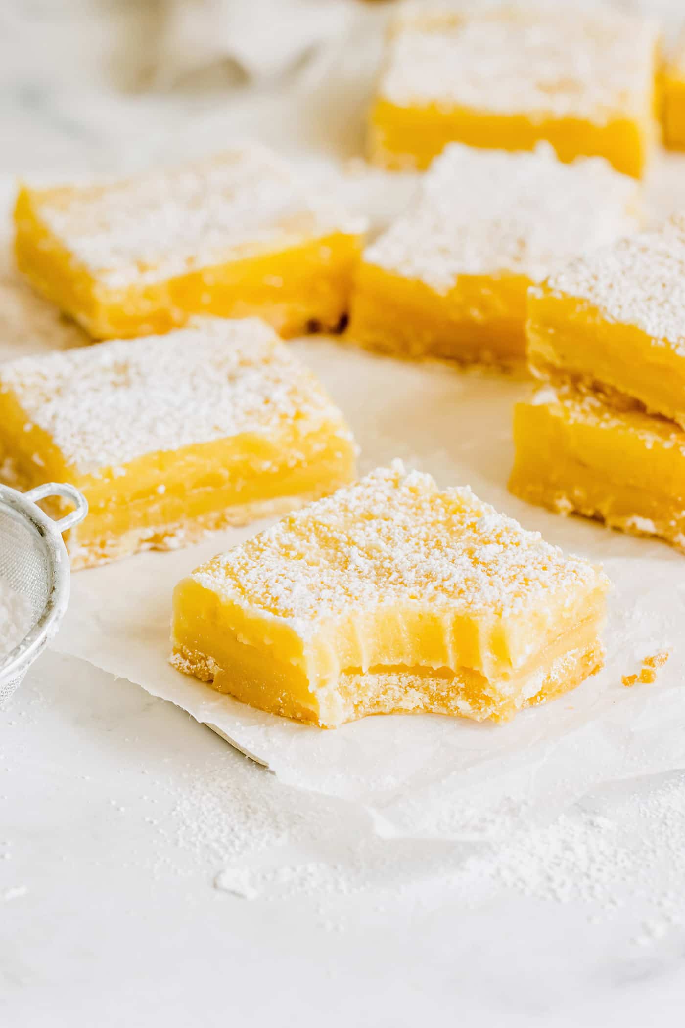 This easy lemon bars recipe is loaded with fresh lemon flavor in a buttery shortbread crust. Only 4 ingredients in the lemon curd filling! a bite out of a lemon bar, plus more lemon bars in the background