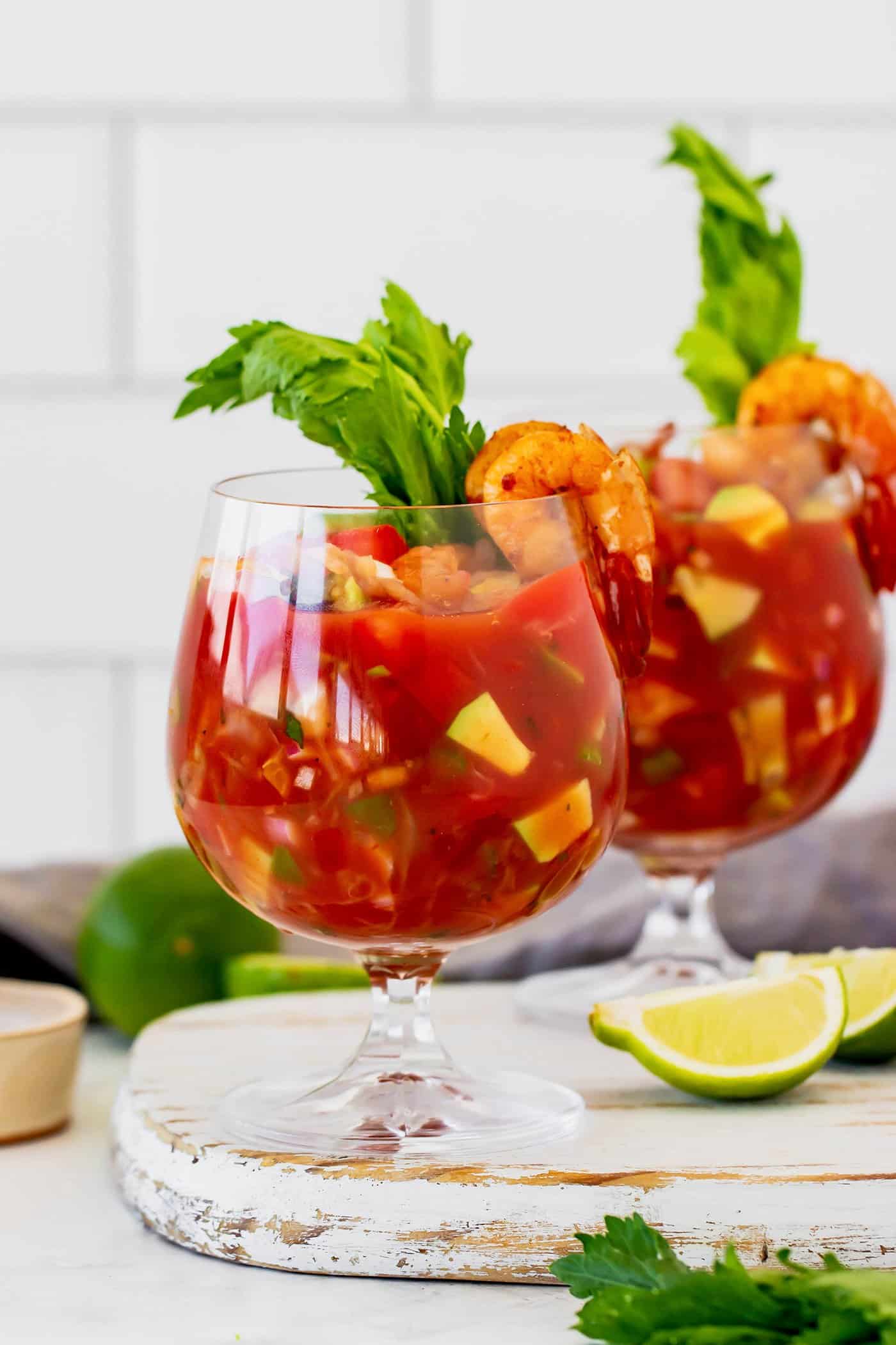 This Mexican shrimp cocktail recipe is a fun twist on a classic appetizer, featuring juicy shrimp and a spicy homemade cocktail sauce! two stemmed glasses with Mexican shrimp cocktail, plus fresh limes