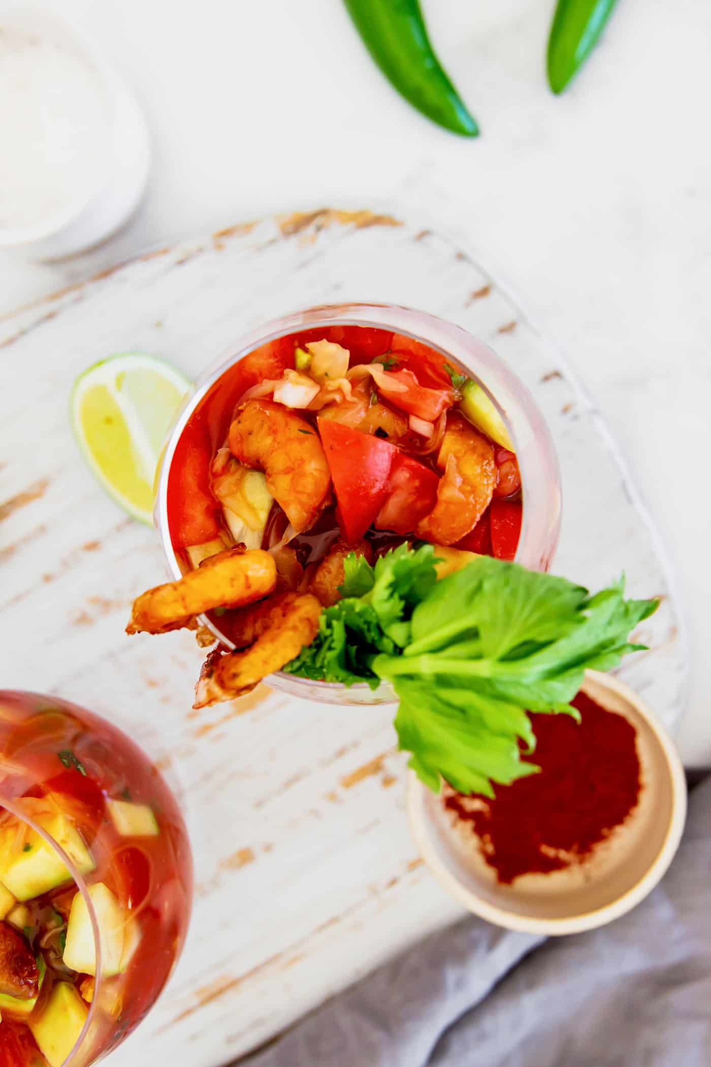 This Mexican shrimp cocktail recipe is a fun twist on a classic appetizer, featuring juicy shrimp and a spicy homemade cocktail sauce! overhead photo of two glasses of appetizers with tomato juice, lime, and shrimp