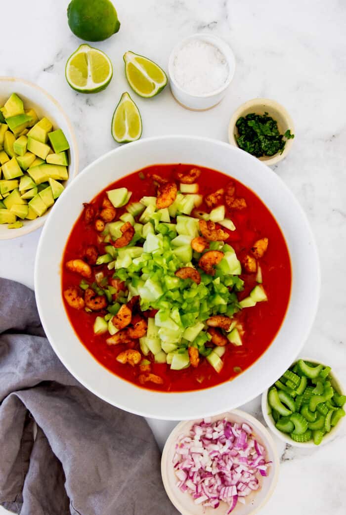 This Mexican shrimp cocktail recipe is a fun twist on a classic appetizer, featuring juicy shrimp and a spicy homemade cocktail sauce! combining a red cocktail sauce with cooked shrimp and diced vegetables in a large white bowl