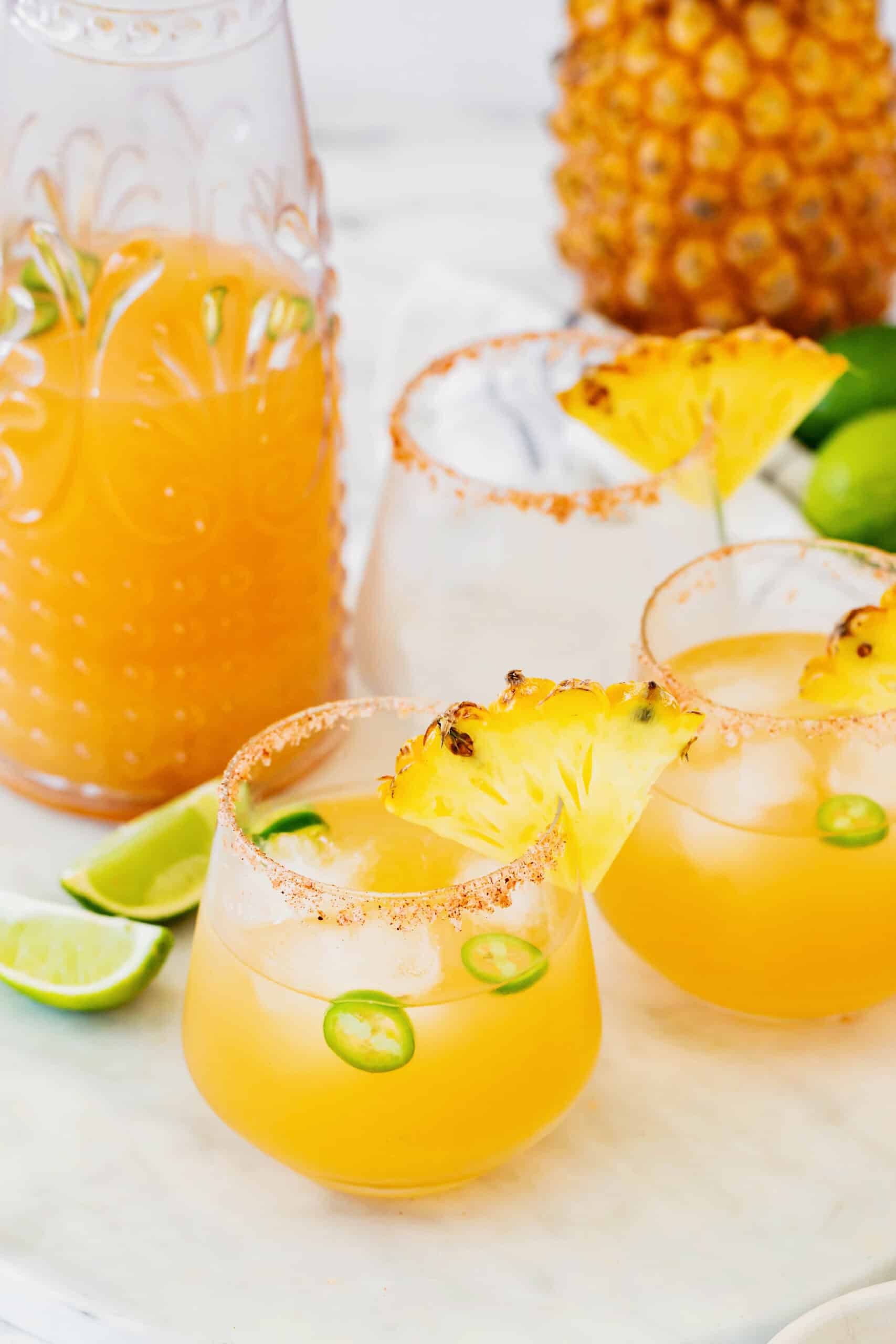 This spicy pineapple jalapeño margarita is a delicious twist on the classic cocktail with blanco tequila, fresh pineapple juice, and jalapeño. a pitcher and three glasses of pineapple margaritas with jalapenos