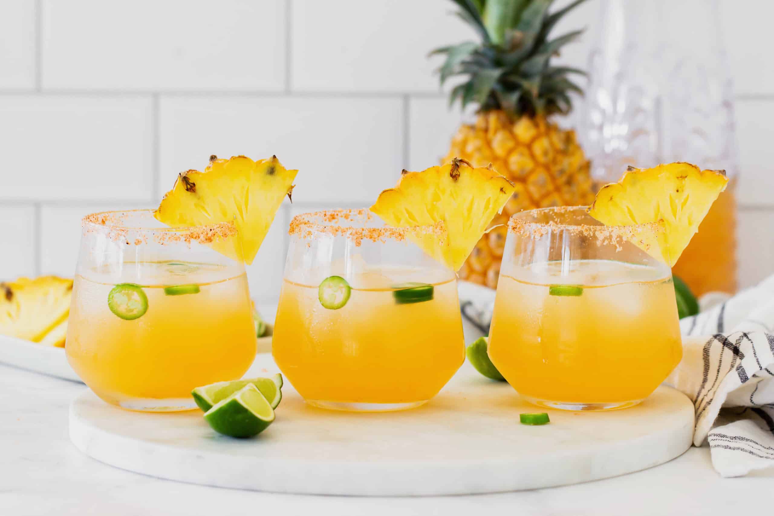 This spicy pineapple jalapeño margarita is a delicious twist on the classic cocktail with blanco tequila, fresh pineapple juice, and jalapeño. 3 glasses of pineapple jalapeno margaritas, arranged in a straight row