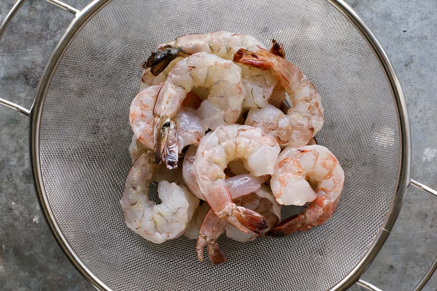 This watermelon and citrus shrimp ceviche recipe is loaded with nuggets of fresh shrimp, plus the bright flavors of orange and lime! raw shrimp in a colander