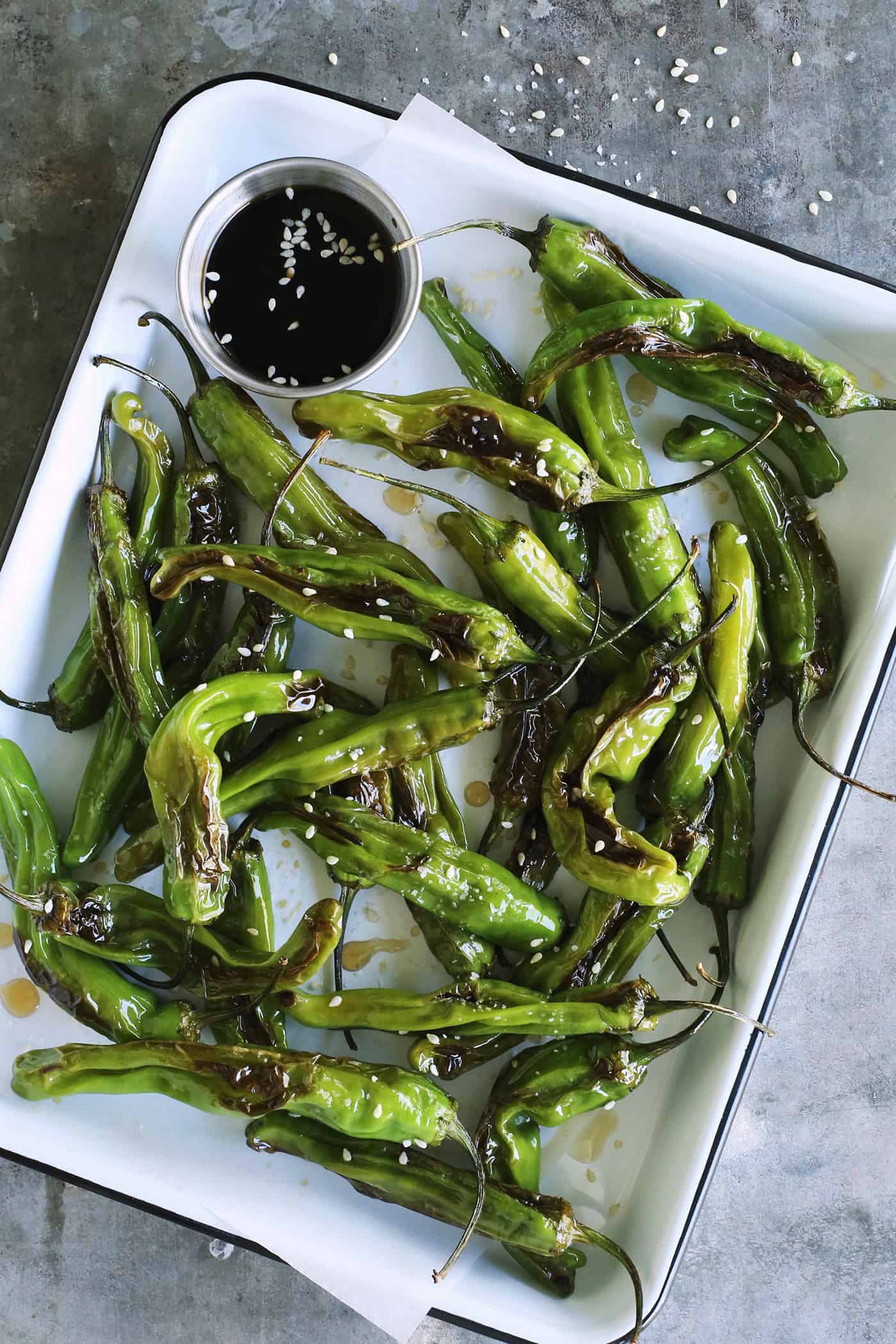 This Blistered Shishito Peppers recipe comes together quickly, with just a few ingredients - one of the easiest appetizers you'll ever make! blistered shishitos on a rectangular white enamel pan