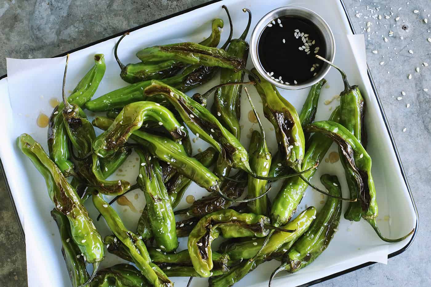 This Blistered Shishito Peppers recipe comes together quickly, with just a few ingredients - one of the easiest appetizers you'll ever make! blistered shishitos on a rectangular white enamel pan with soy honey sauce