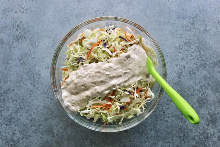 This crunchy, creamy coleslaw recipe is a favorite BBQ side. Serve it as a cooling accompaniment to grilled meats, tacos, or pulled pork! creamy dressing poured over shredded coleslaw mix in a clear bowl