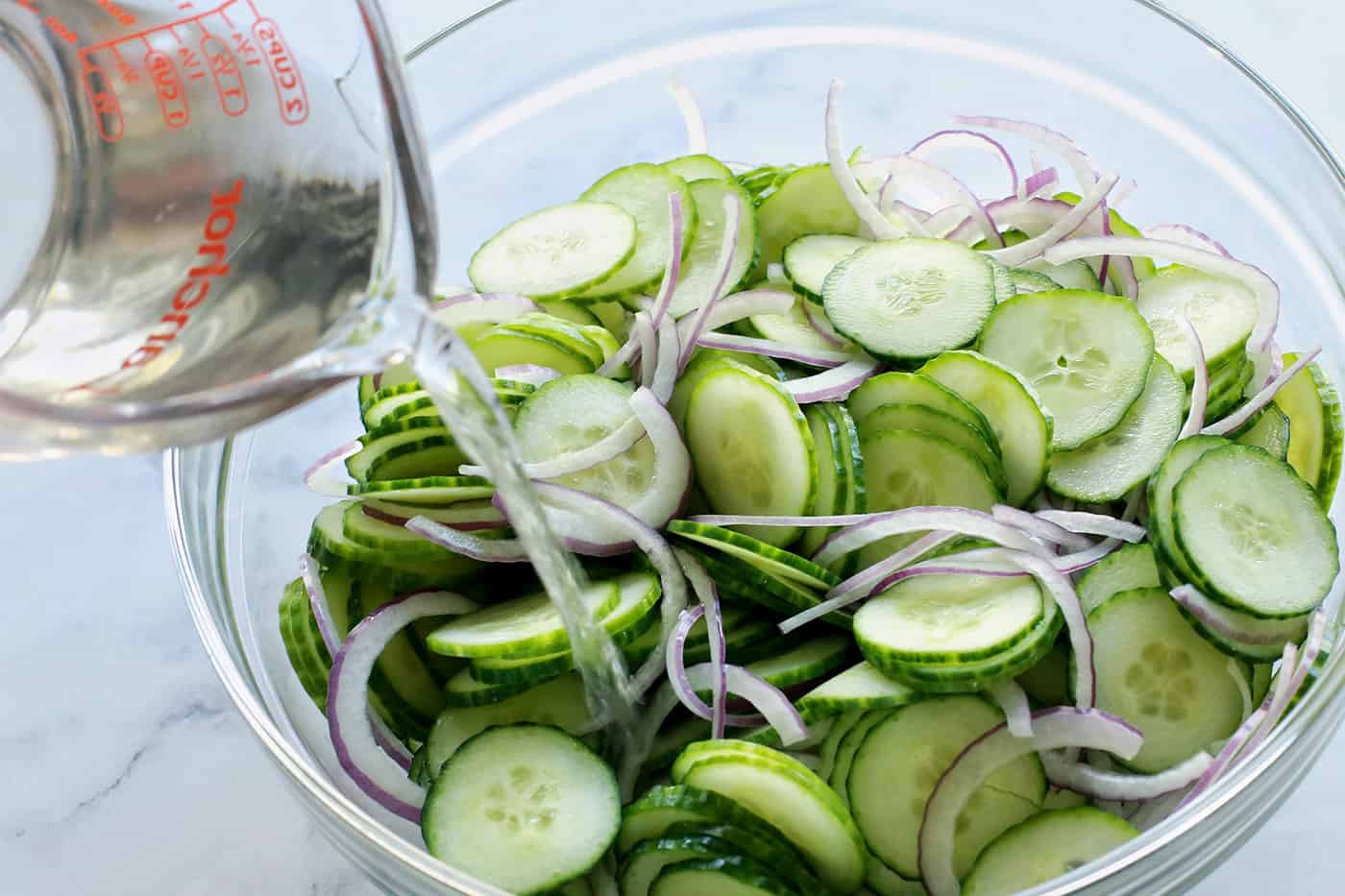 This easy cucumber salad recipe is a refreshing summertime side dish with thinly sliced cucumbers and onion, plus a tangy vinegar dressing. pouring vinegar mixture over sliced cucumbers and red onion in a clear bowl