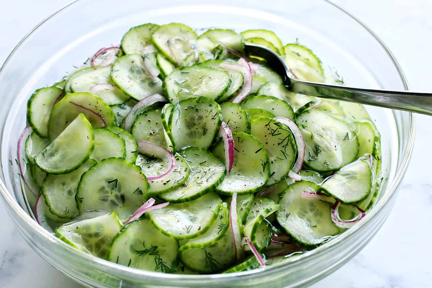 This easy cucumber salad recipe is a refreshing summertime side dish with thinly sliced cucumbers and onion, plus a tangy vinegar dressing. cucumber and onion salad with vinegar dressing in a large clear bowl, with a serving spoon