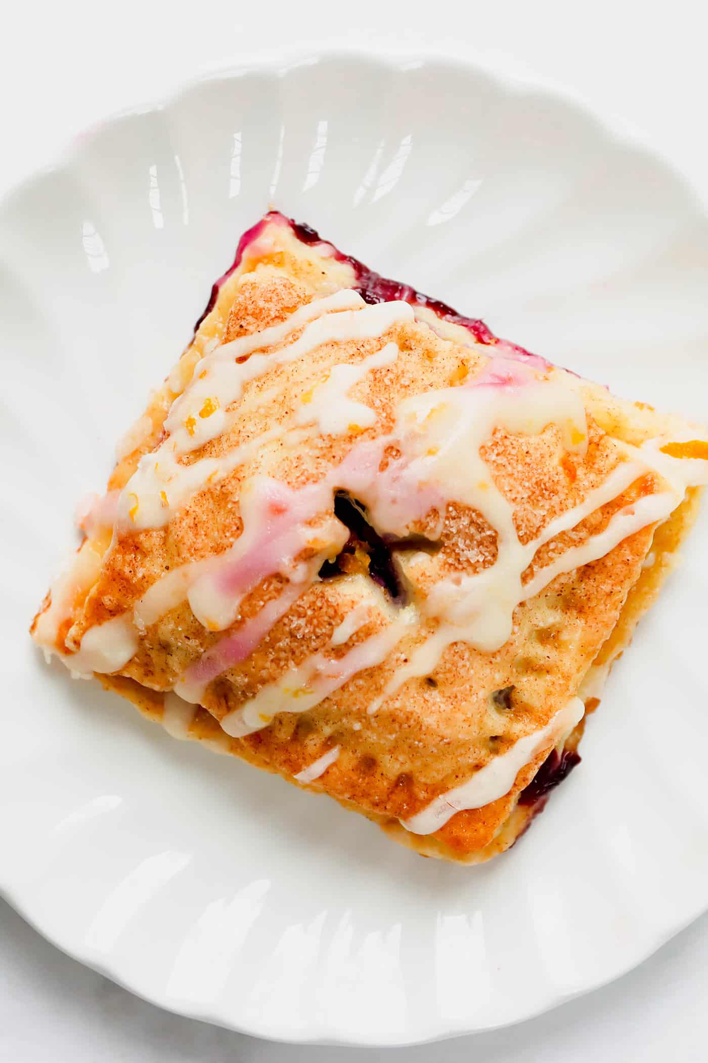 These cute blueberry hand pies combine a flaky pastry crust with sweet blueberry pie filling. It's so much easier than baking a whole pie! Overhead view of a blueberry hand pie on a white plate, drizzled with a fresh orange glaze.