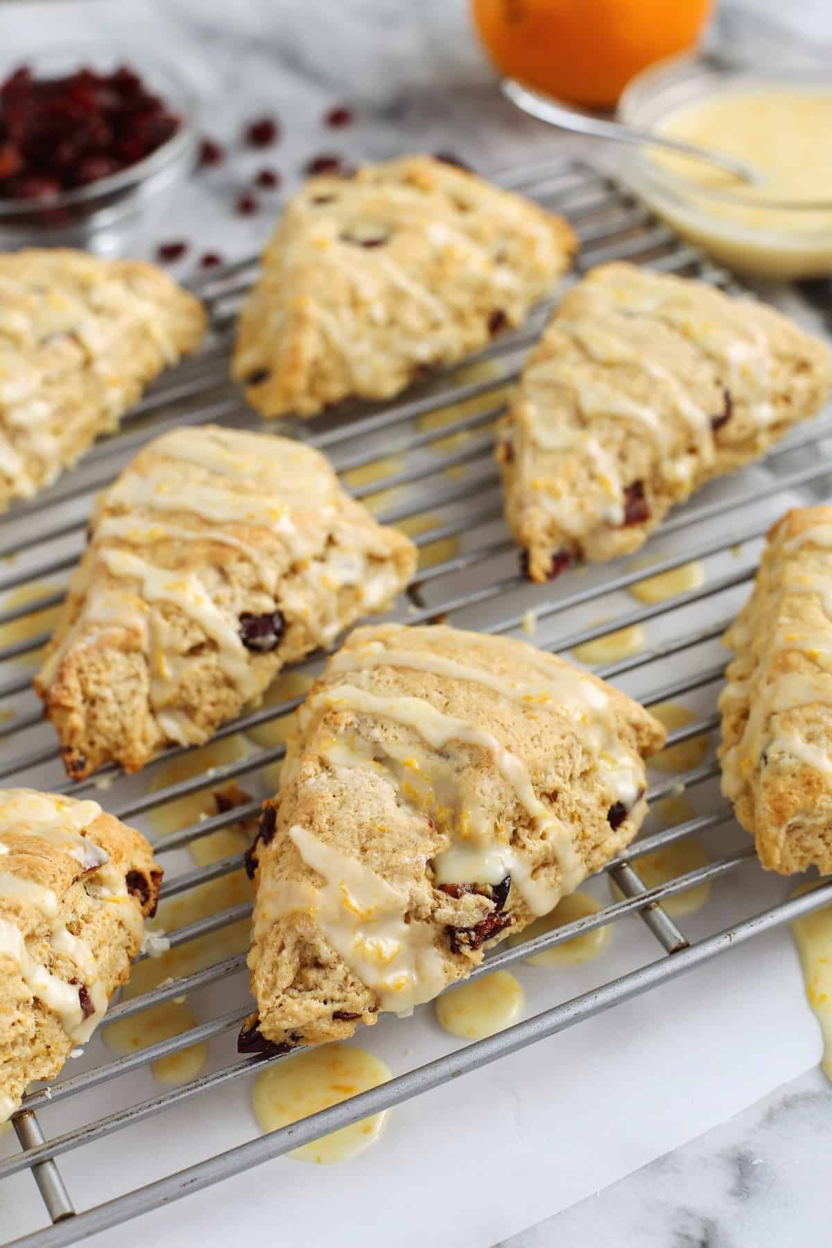 These homemade cranberry orange scones are perfectly flaky and great for a weekend breakfast or holiday brunch. They're easy to make too! Glazed cranberry orange scones on a wire rack with a bowl of glaze in the background.