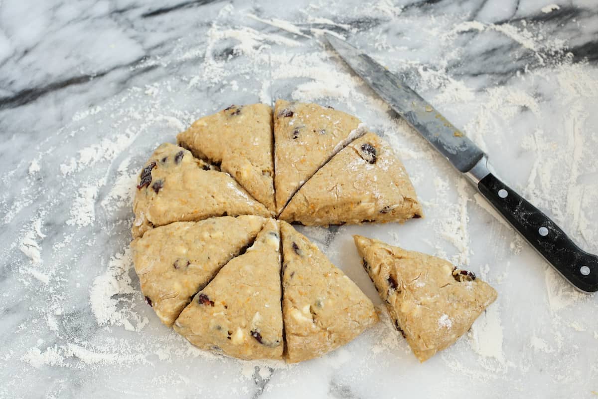 These homemade cranberry orange scones are perfectly flaky and great for a weekend breakfast or holiday brunch. They're easy to make too! Scone dough cut into wedges on a marble countertop next to a large knife.