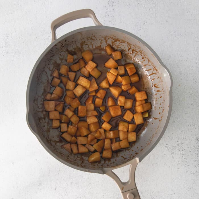 Overnight baked apple oatmeal is an irresistible make-ahead breakfast, topped with crunchy streusel and studded with sweet cinnamon apples. Chopped cinnamon apples sauteeing in a skillet.