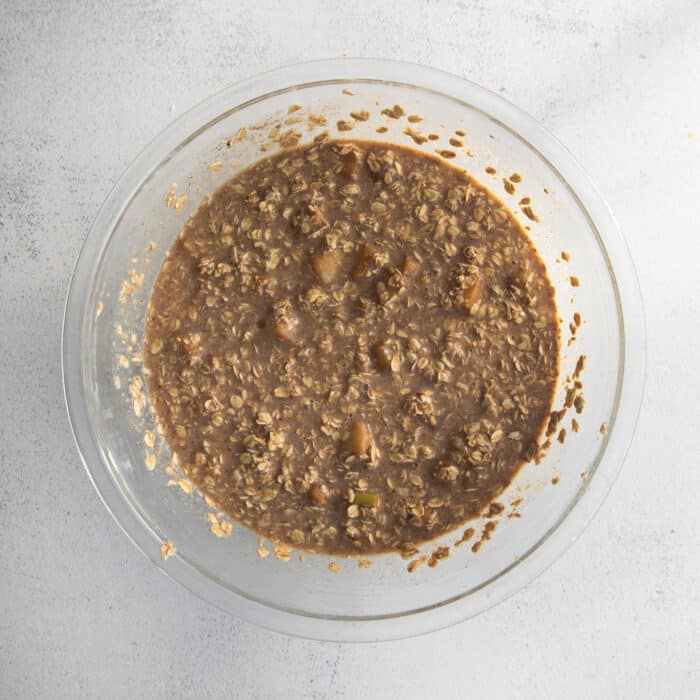 Overnight baked apple oatmeal is an irresistible make-ahead breakfast, topped with crunchy streusel and studded with sweet cinnamon apples. Apple oatmeal in a glass mixing bowl.