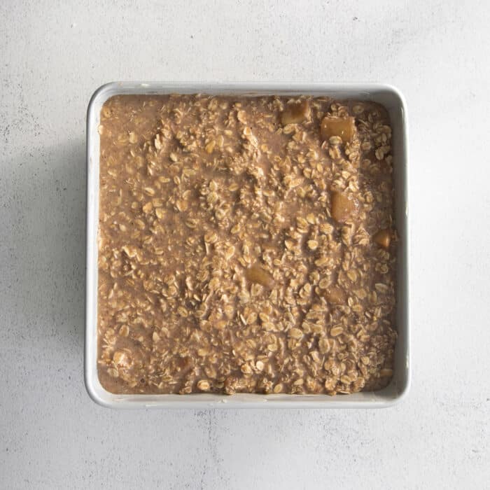 Overnight baked apple oatmeal is an irresistible make-ahead breakfast, topped with crunchy streusel and studded with sweet cinnamon apples. Overhead view of unbaked apple oatmeal in a white ceramic baking dish.