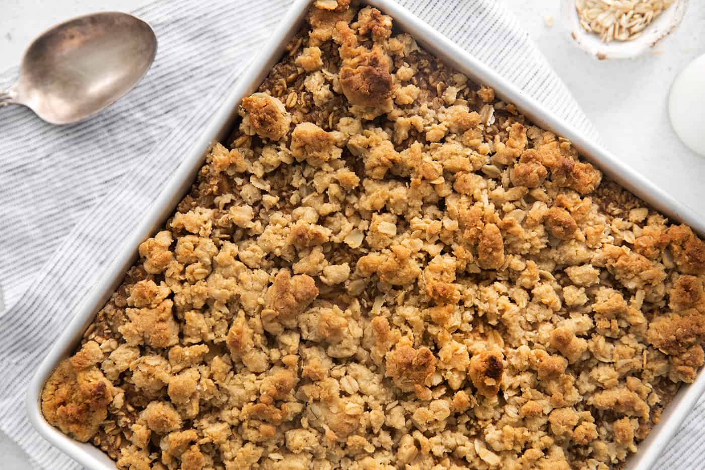 Overnight baked apple oatmeal is an irresistible make-ahead breakfast, topped with crunchy streusel and studded with sweet cinnamon apples. Overhead view of baked apple oatmeal in a white ceramic baking dish.