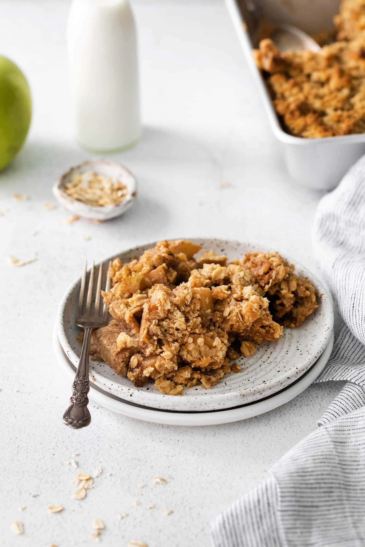 Overnight baked apple oatmeal is an irresistible make-ahead breakfast, topped with crunchy streusel and studded with sweet cinnamon apples. A serving of baked oatmeal with cinnamon apples on a small plate.