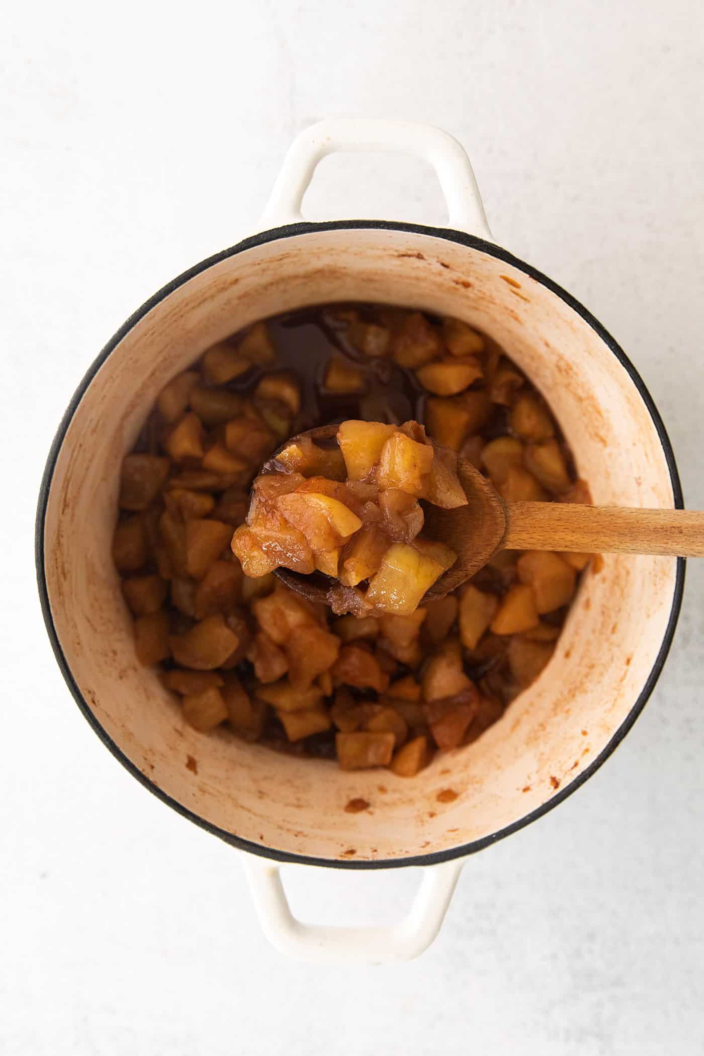 This easy homemade applesauce recipe can be made smooth or chunky, with simple refrigerator storage or canning for long-term pantry storage! a wooden spoonful of homemade applesauce out of a large white pot