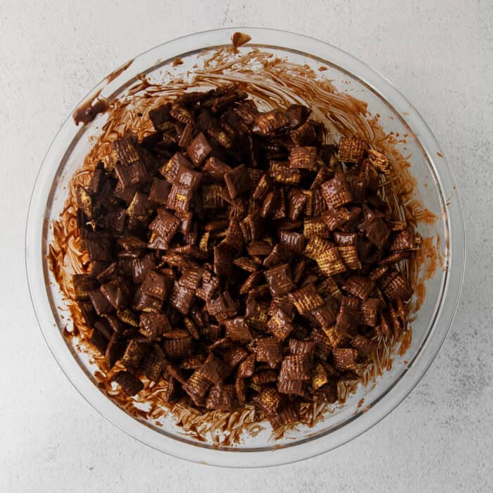 A large clear bowl of Chex cereal covered in a melted chocolate and peanut butter mixture.