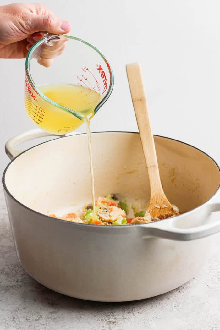 Pouring broth from liquid measuring cup into Dutch oven