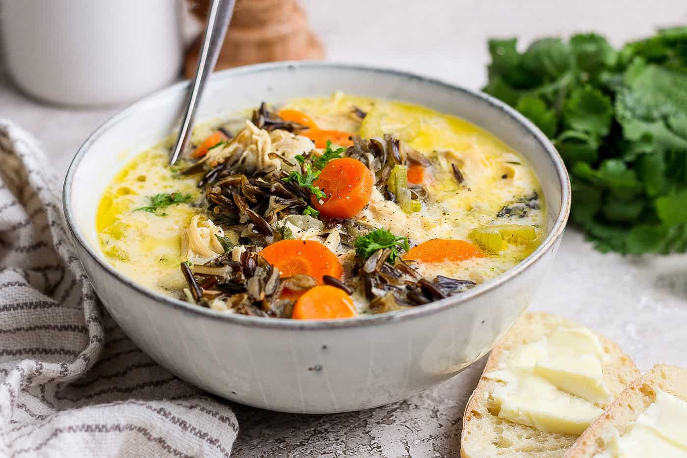 Bowl of chicken wild rice soup with buttered bread slices in foreground