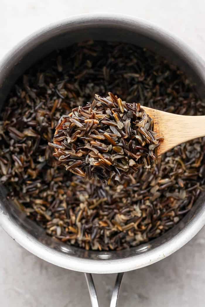 Wooden spoon with wild rice, held over pot with additional rice