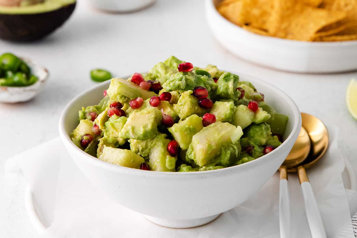 With sweet pops of fruit and pomegranate seeds, this Holiday Guacamole is a quick and festive party appetizer! Delicious with tortilla chips! A bowl of holiday guacamole with a bowl of tortilla chips in he background.