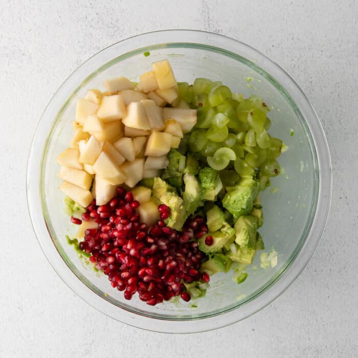 With sweet pops of fruit and pomegranate seeds, this Holiday Guacamole is a quick and festive party appetizer! Delicious with tortilla chips! Avocado, pomegranate seeds, and pears combined in a glass bowl.