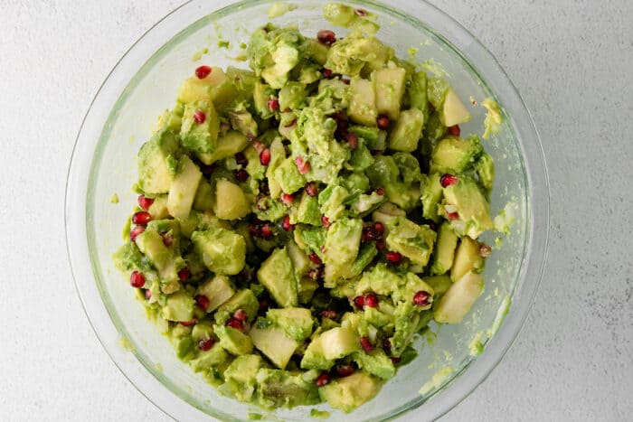 With sweet pops of fruit and pomegranate seeds, this Holiday Guacamole is a quick and festive party appetizer! Delicious with tortilla chips! Holiday guacamole mixed in a glass bowl.