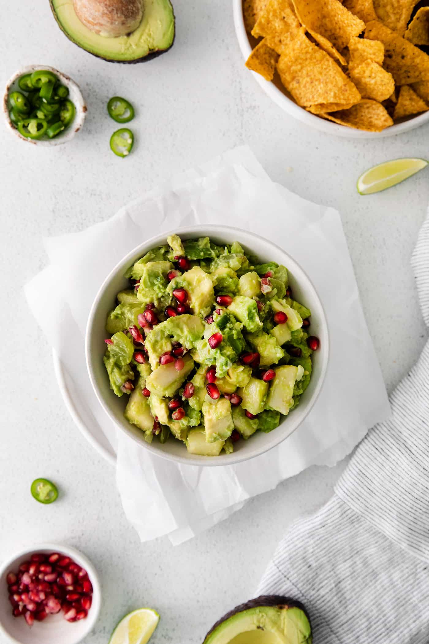With sweet pops of fruit and pomegranate seeds, this Holiday Guacamole is a quick and festive party appetizer! Delicious with tortilla chips! Overhead view of a bowl of Christmas guacamole next to a bowl of tortilla chips.