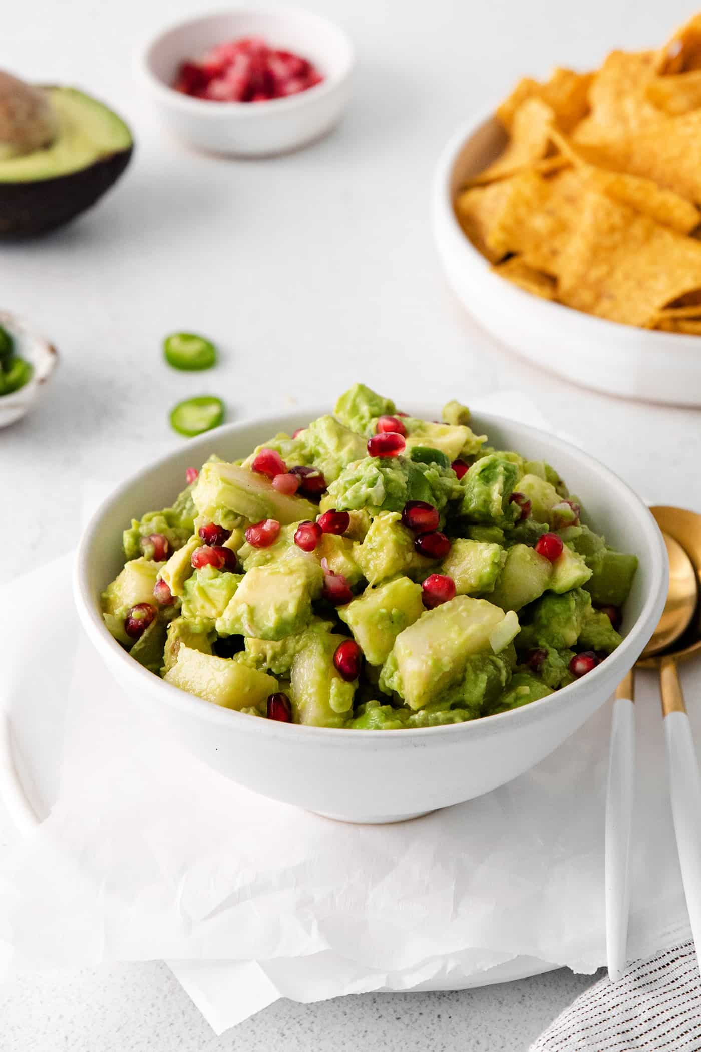 With sweet pops of fruit and pomegranate seeds, this Holiday Guacamole is a quick and festive party appetizer! Delicious with tortilla chips! A bowl of Christmas guacamole with a bowl of tortilla chips in he background.