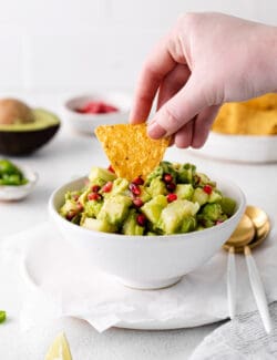 A hand dipping a chip into a bowl of holiday guacamole.