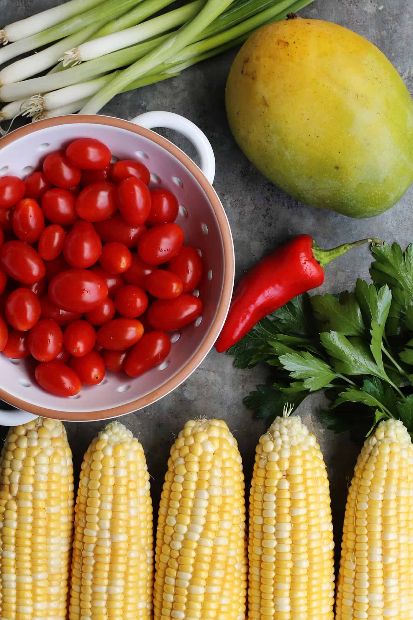 With fresh corn, mangos, tomatoes, and a touch of heat, plus a light and flavorful dressing, this Sweet Corn Salad is a summer treat! fresh ingredients for salad: sweet corn, mango, tomatoes, chili, green onion, parsley