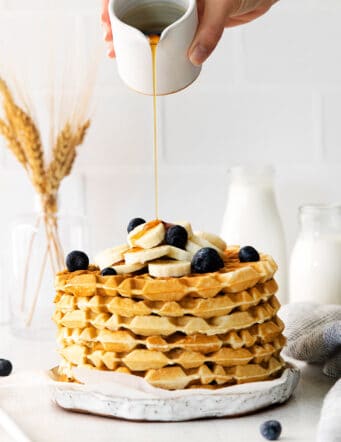 SYrup being poured over a stack of classic waffles topped with blueberries and bananas
