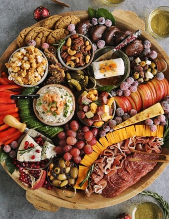 a large round wood charcuterie board full of cheese, meat, olives, sweets, and nuts